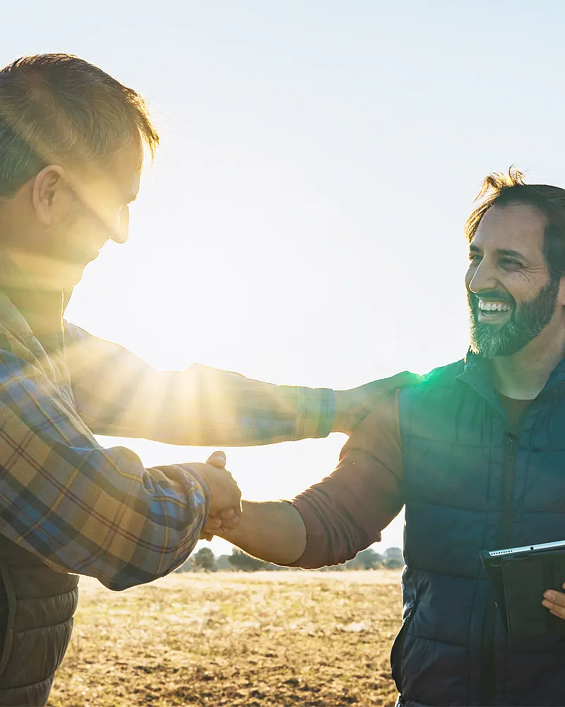 农业中的可信合作伙伴关系 – 两人在田间握手，象征着在农业技术方面的长期经验。