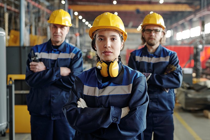 3 workers with blue overalls and yellow helmets in a production hall