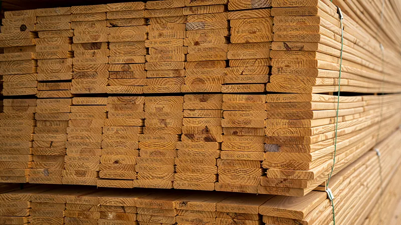 Close-up view of neatly stacked kiln-dried wooden planks, showing clear growth rings and stamped markings on the end grain.