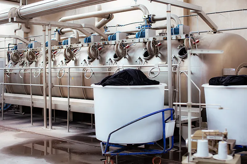 配有大型不锈钢染色机和布料桶的工业纺织品烘干设备。